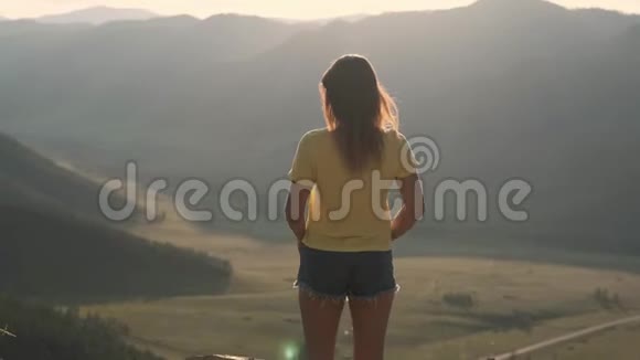 日落时分一位年轻女子站在悬崖边上双手举在高高的岩石山前视频的预览图