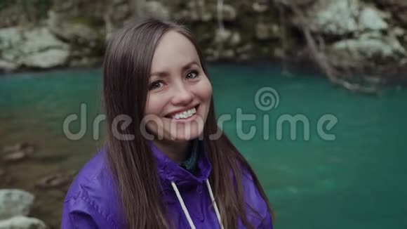 可爱的快乐女孩看着镜头在一个绿松石山湖的背景上笑得很宽视频的预览图
