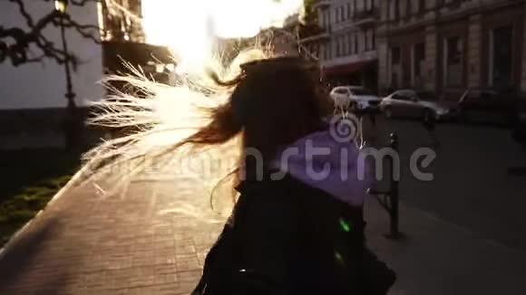 开朗长发的女孩穿着黑色皮夹克走着甚至穿过充满阳光的城市街道女孩视频的预览图