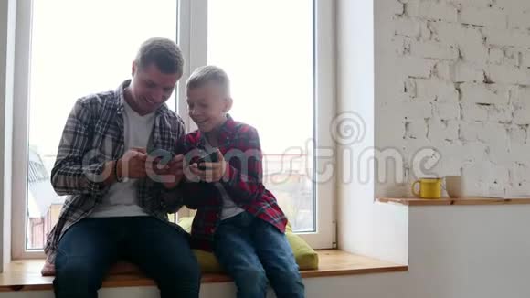 快乐的父子用智能手机在窗台上放松视频的预览图