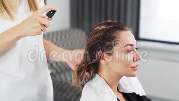 美容师将护理产品应用于美容店年轻女性的湿发视频的预览图