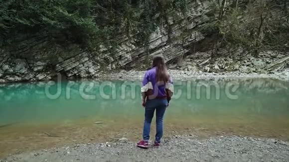 穿着休闲风格的女孩站在山上一个干净的蓝色湖泊的岸边放大了视频的预览图