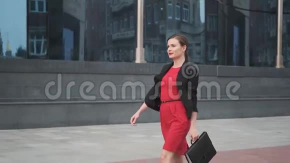自信的商务女性穿着红色连衣裙走在商务中心旁边穿红色裙子的年轻女子视频的预览图