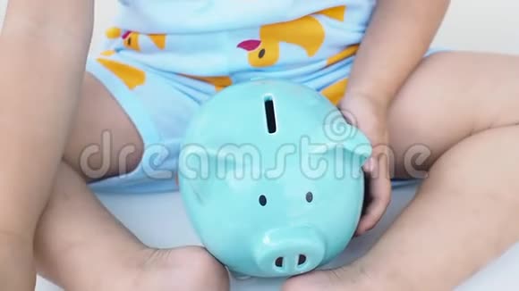 一个孩子正在把硬币放在蓝色的储蓄罐里为未来的概念储蓄儿童教育视频的预览图