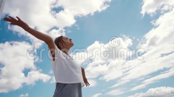 年轻快乐的女人在白云和明亮的蓝天的背景下举手视频的预览图