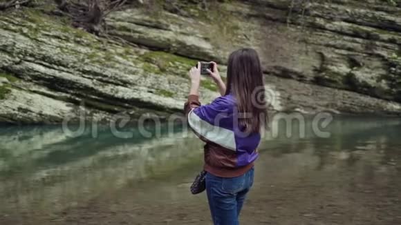 穿着运动夹克的女孩在电话里拍下了山湖的美丽景色视频的预览图
