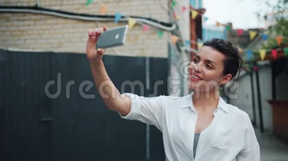 漂亮女士在外面用智能手机摆手自拍的慢动作视频的预览图