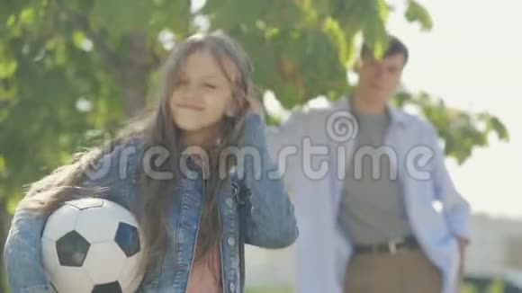 可爱有趣的小女孩站在她哥哥的背景上带着足球微笑的画像视频的预览图