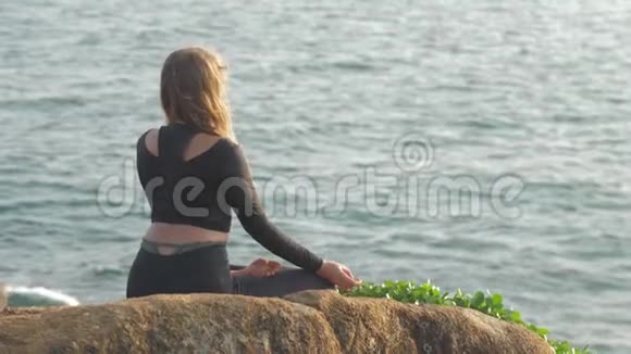 穿着运动服的布鲁内特坐在灰色的岩石悬崖上冥想视频的预览图