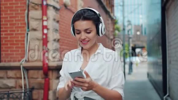 使用智能手机在户外行走时在耳机中欣赏音乐的女士肖像视频的预览图