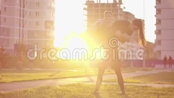 一个男人蹲在城市公园里一个女孩坐在他的肩膀上背景是日落时的建筑物视频的预览图
