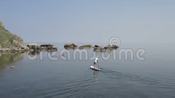 冲浪者在白色的冲浪板上漂浮在平静的清澈的水面上美丽的夏日视频的预览图