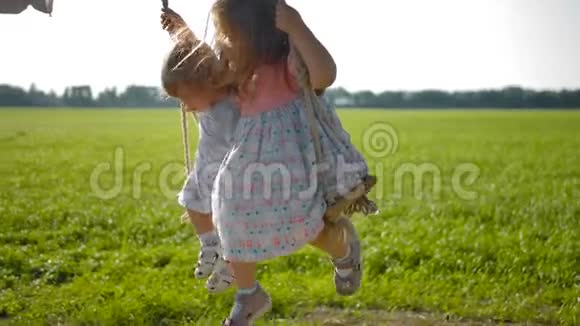 两个穿着可爱裙子的小女孩在秋千上摇摆快乐地晃着脚视频的预览图