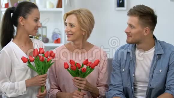 年迈的母亲和妻子手持郁金香花束坐在男性身边对着镜头微笑视频的预览图