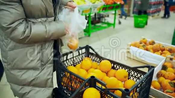 一个穿冬衣的女人把橘子放进袋子里为圣诞节或假日购买水果一个在超市里的女人视频的预览图