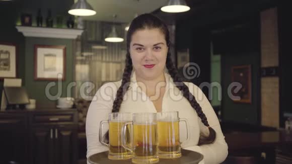 一个梳着辫子的女人穿着白色衬衫拿着托盘带着三个啤酒杯对着镜头微笑男性手视频的预览图