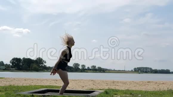 年轻性感的金发女郎在户外慢动作的蹦床里在空中缠绕视频的预览图