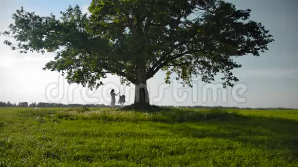 孤独美丽的大树和妈妈的小剪影两个女儿荡秋千视频的预览图
