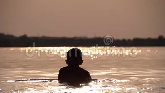 日落时分快乐男孩潜入河中的剪影慢动作视频的预览图
