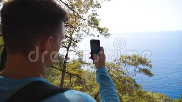 年轻人在他的智能手机上拍摄风景优美的海景他用电话从希尔那里获取美丽的海洋图片视频的预览图