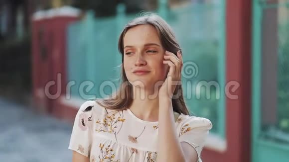 年轻迷人的女孩棕色头发蓝眼睛穿着白色的花裙在绿松石围栏附近微笑视频的预览图
