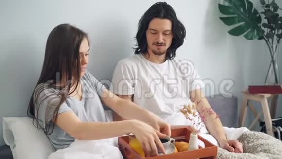 美丽的一对夫妇在家里的床上吃早餐喝咖啡果汁糕点视频的预览图