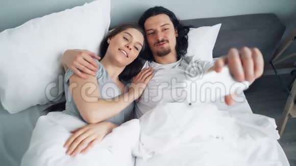 大胡子男和女友用智能手机摄像头在床上自拍视频的预览图