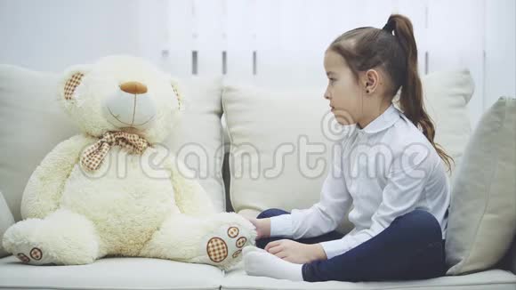 可爱的小女孩坐在沙发上和她的泰迪说话礼貌地解释双手折叠看着视频的预览图