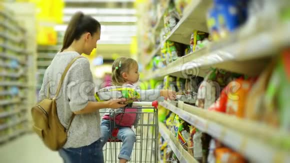 年轻漂亮的妈妈和小孩在超市买食物美丽的女人可爱的女孩站在架子旁视频的预览图
