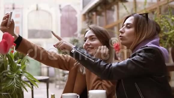 女朋友坐在咖啡馆里用手机相机自拍两个迷人的女孩在相机上拍照视频的预览图