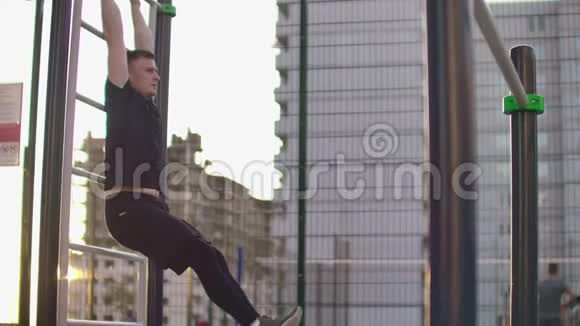 一名男子在城市公园的建筑物背景下在双杠上缓慢地表演抬腿动作视频的预览图