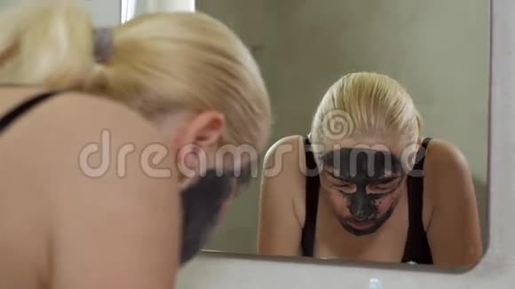 一个女人站在洗手池附近的浴室里用水龙头里的水洗掉了一个泥浆化妆品面具视频的预览图