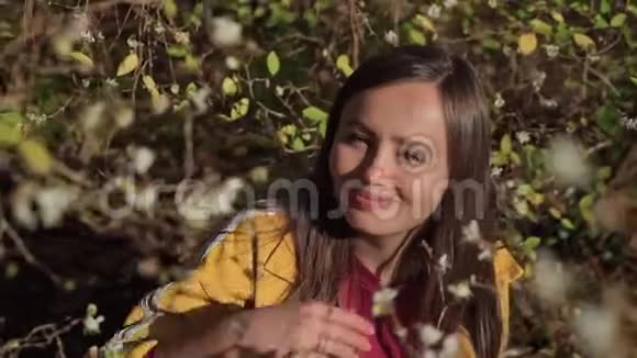 快乐的女孩在灌木的树枝上检查白花她微笑着视频的预览图