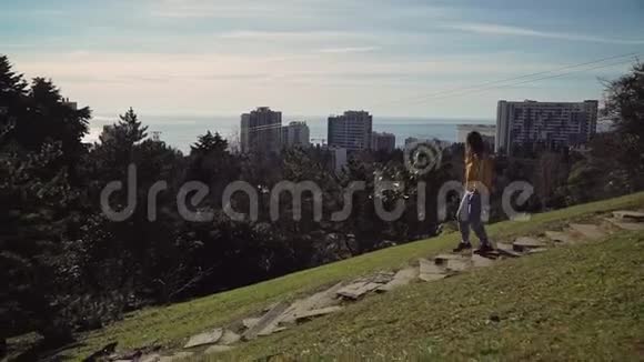 女孩跑下石阶在一座绿色的小山的背景上的高层建筑周围是绿色植物视频的预览图