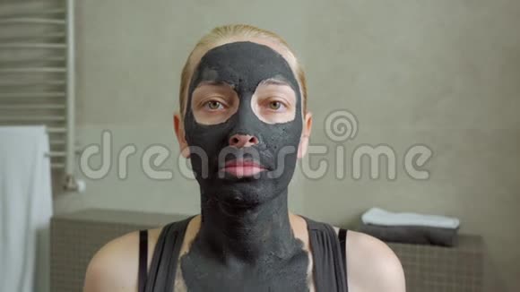 浴室里的一个女人脸上戴着黑色的泥面罩看着镜子里的自己视频的预览图