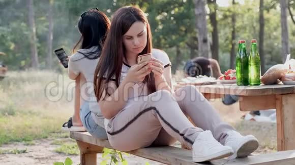 两个年轻女孩在野餐时用一种呆滞的眼神看着她们的手机而她们的男朋友则生火做饭视频的预览图