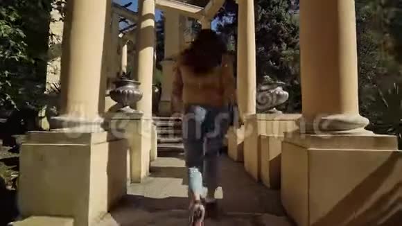 在一个美丽的公园里一个年轻的女人跑上带有古董柱子的石阶视频的预览图