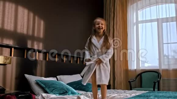 一个留着长发的小女孩在旅馆房间的床上蹦蹦跳跳视频的预览图