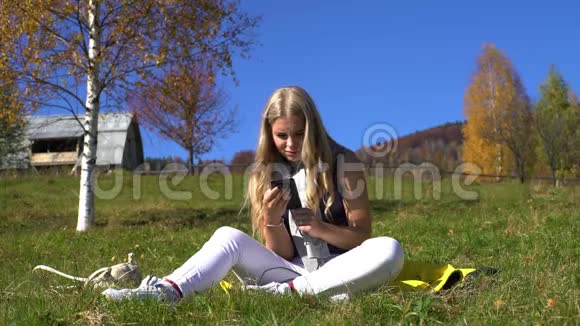 年轻的乡村学生自由职业者女孩在秋山村用手机坐在草地上放松视频的预览图