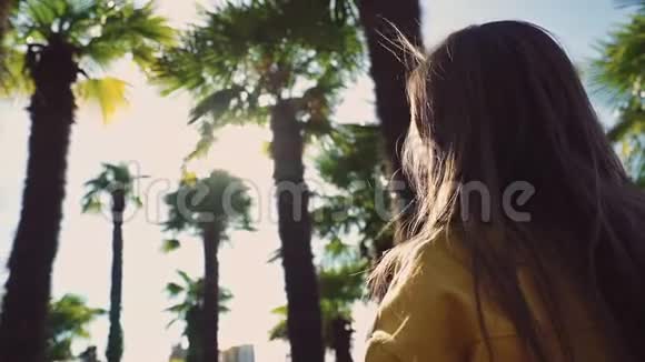 一位身穿黄色夹克衫的长发女孩看到了棕榈树的美丽景色并开始在一张照片上拍照视频的预览图
