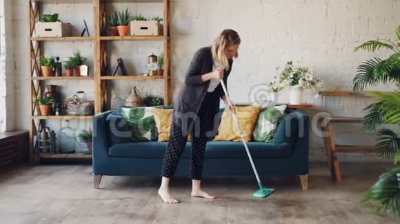 漂亮的金发家庭主妇正在做家务在漂亮的平面清洁沙发下拖地女孩是视频的预览图