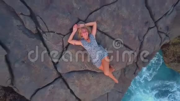 美丽的女孩躺在靠近蔚蓝海洋的悬崖上鸟瞰视频的预览图