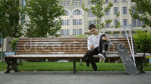 有魅力的年轻人坐在公园的长凳上用手机听音乐然后拿起拐杖和拐杖视频的预览图