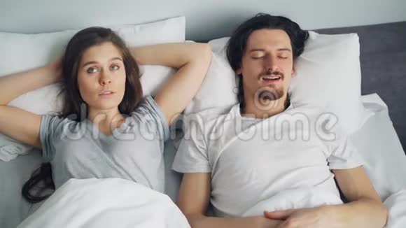 愤怒的妻子一边睡觉一边用枕头遮住脸丈夫在床上打鼾视频的预览图