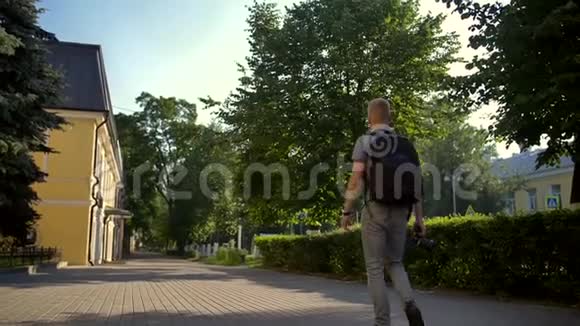 年轻的摄影师走在他身后的一条城市街道上视频的预览图