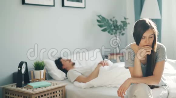 不高兴的女孩坐在床上想着当男人醒来时拥抱和亲吻视频的预览图