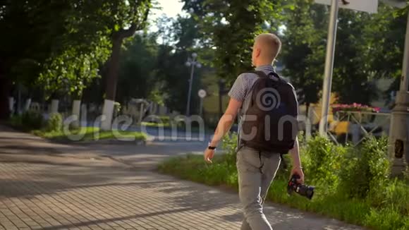 一位背着黑色背包的学生摄影师正沿着一条街散步视频的预览图