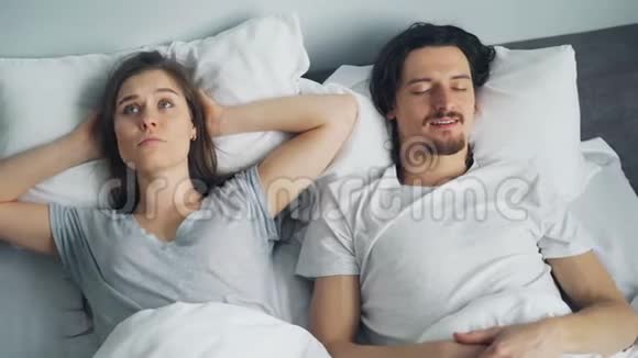 丈夫在床上打鼾时不高兴的女孩用枕头捂住耳朵视频的预览图