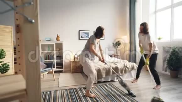可爱的情侣用吸尘器清洁地板用拖把跳舞唱歌视频的预览图