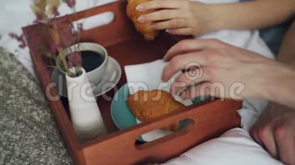 年轻人从托盘里拿食物和饮料在床上享受早餐笑着视频的预览图